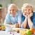 Zwei Senioren lehnen auf einem Küchentisch auf dem Früchte liegen.