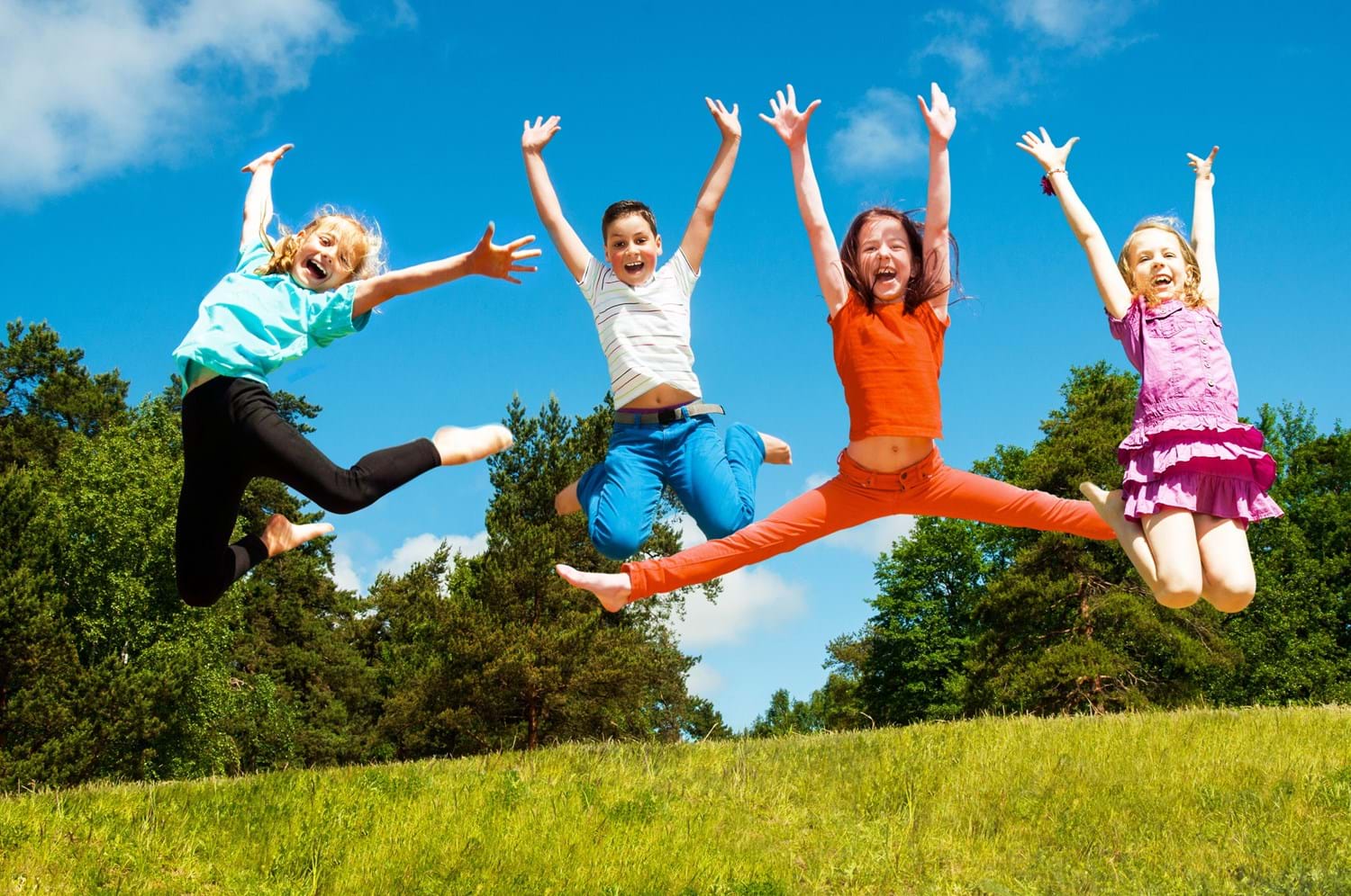 Kinder auf einer Wiese springen gemeinsam in die Luft und halten dabei die Hände in die Höhe.