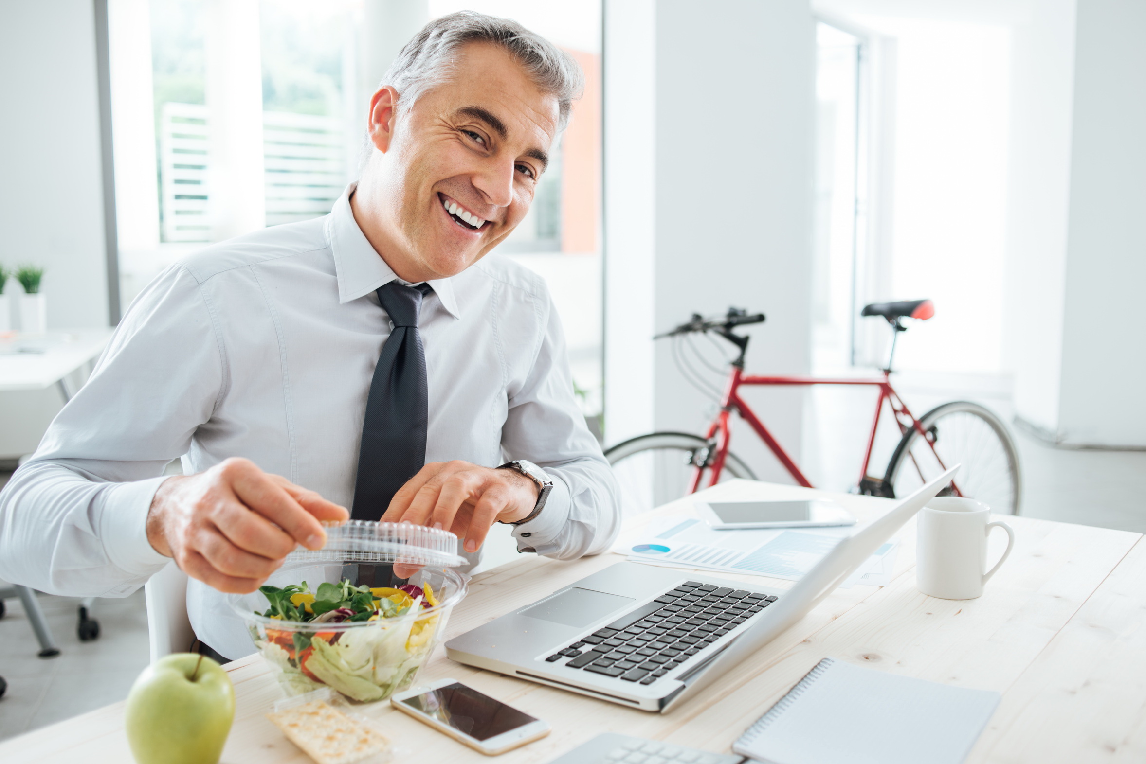 BGF - stock.adobe.com -Fotolia_89908835_L.jpg Mann öffnet am Schreibtisch seine Salatbox