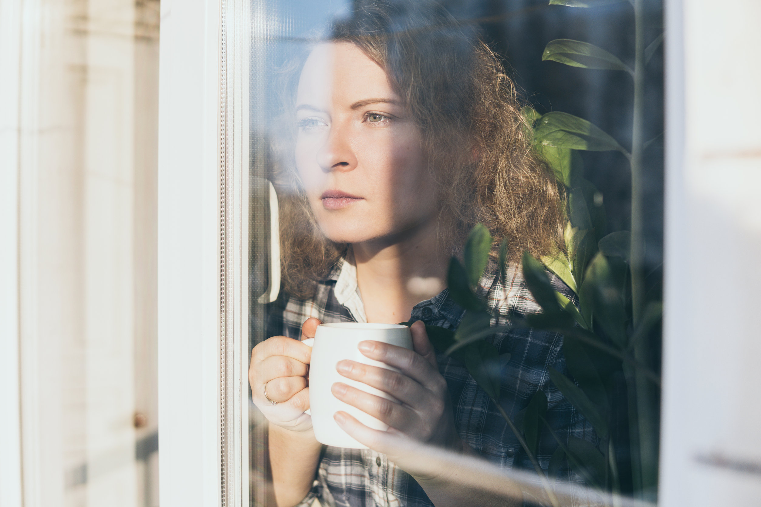 Frau mit Kaffeetasse schaut sehnsüchtig aus dem Fenster