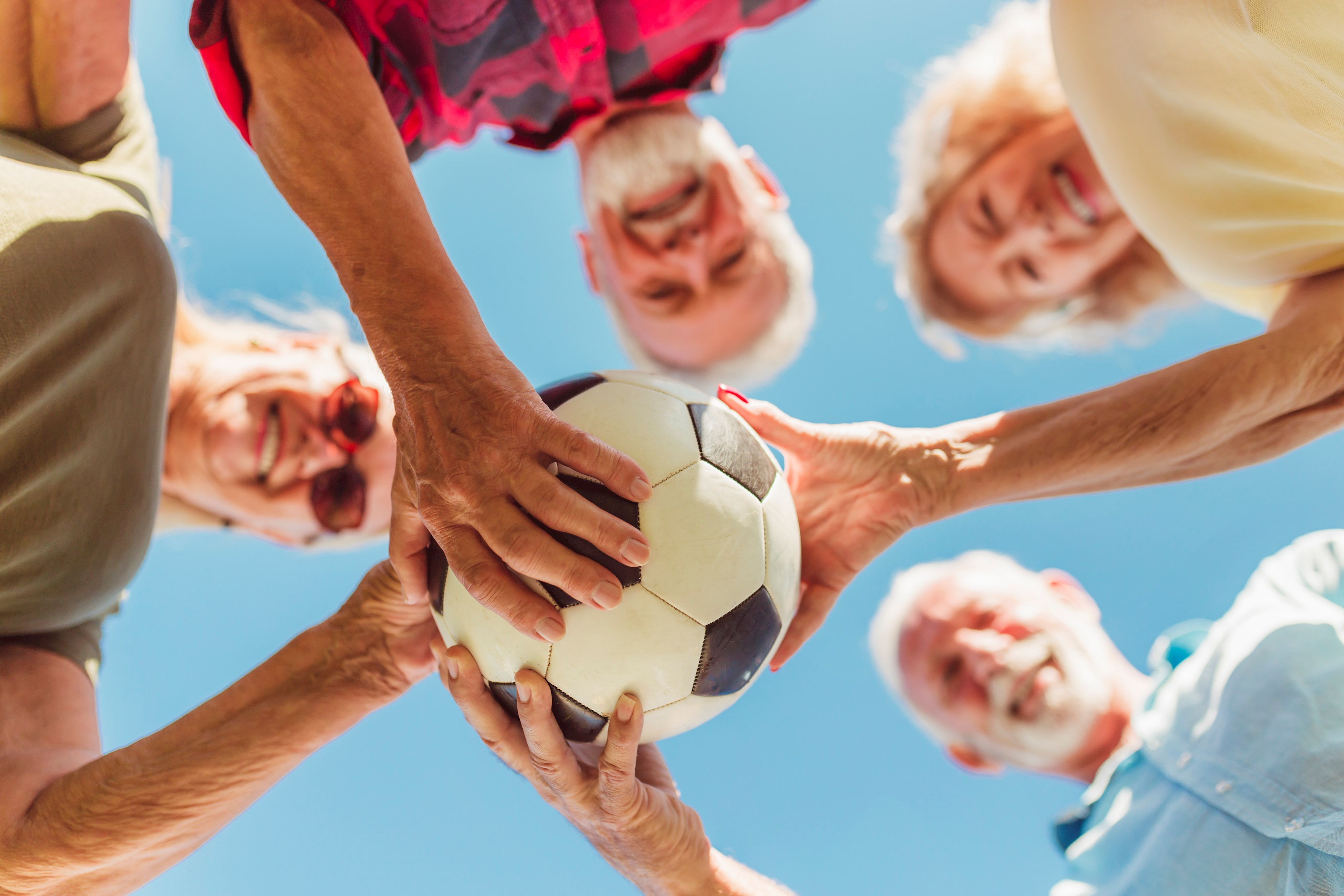 Senioren im Kreis mit einem Fußball blicken nach unten