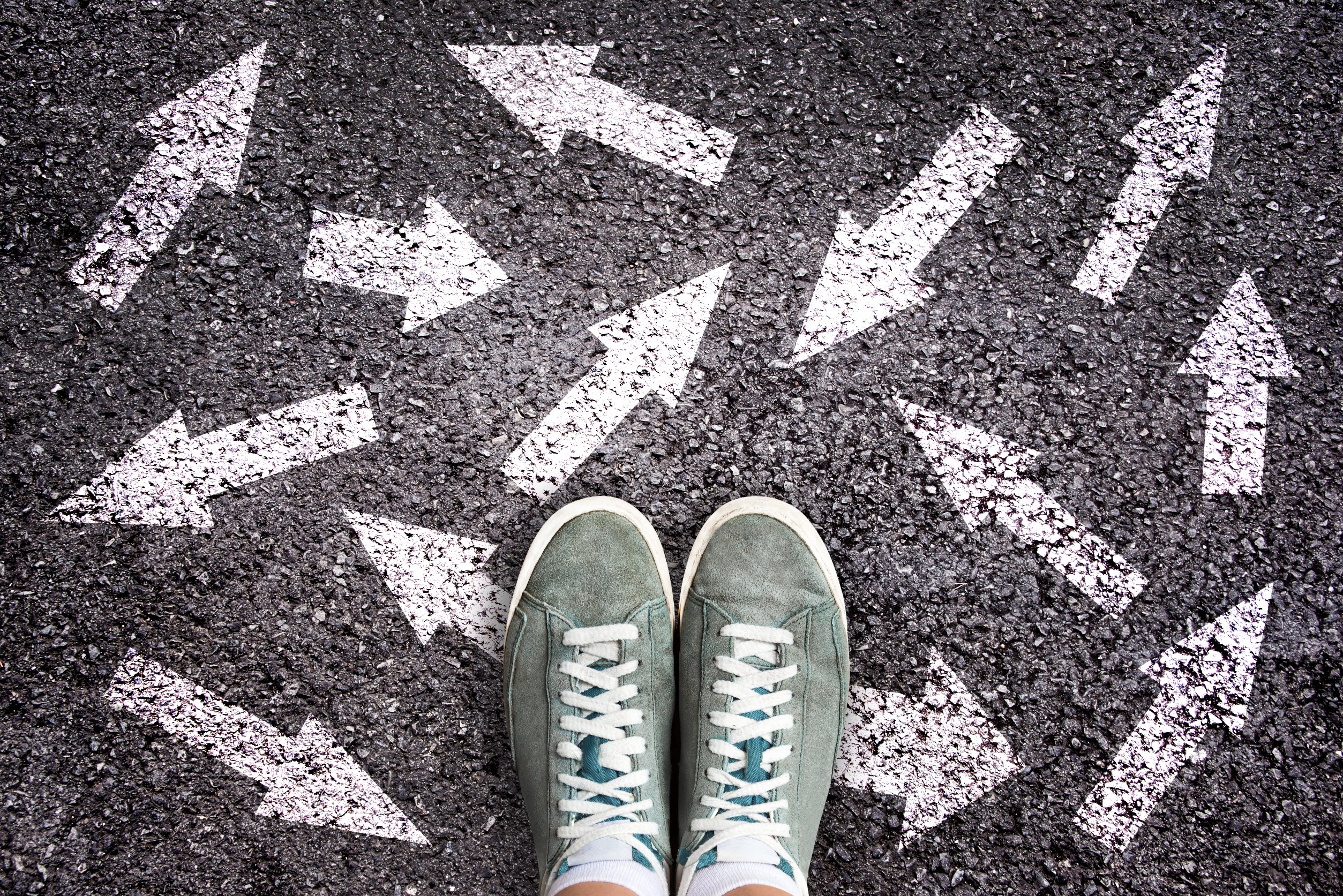 Leider haben wir keinen Titel zu diesem Bild. Wir arbeiten daran und bitten um Ihr Verständnis. Turnschuhe auf Asphalt mit Pfeilen in unterschiedliche Richtungen